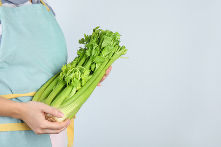 Woman holding fresh green celery on light background, closeup. Space for textの写真素材