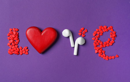 Word Love made with sprinkles, red heart and modern earphones on purple background, flat lay. Listening music songsの写真素材