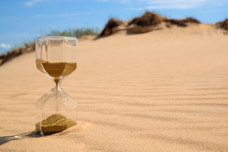 Hourglass with flowing sand in desert on sunny day. Space for textの写真素材