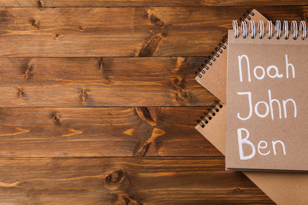 Notebook with different baby names on wooden table, flat lay. Space for textの写真素材