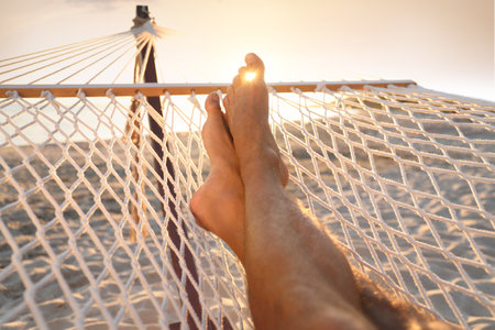 Man relaxing in hammock on beach at sunset, closeupの写真素材