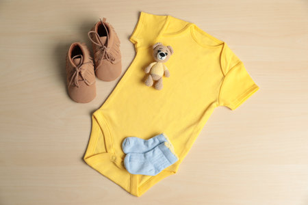 Baby onesie, shoes, socks and toy bear on wooden table, flat layの写真素材