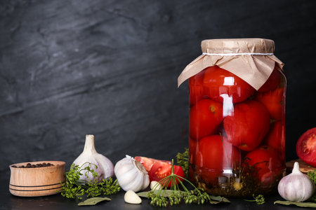 Glass jar of pickled tomatoes and ingredients on black table. Space for textの写真素材