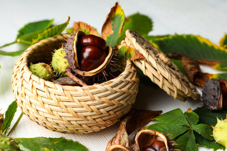 Horse chestnuts in wicker basket on white wooden table, closeupの写真素材