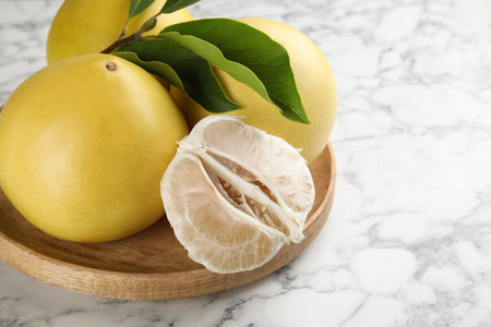Fresh cut and whole pomelo fruits with leaves on white marble table, closeup. Space for textの写真素材