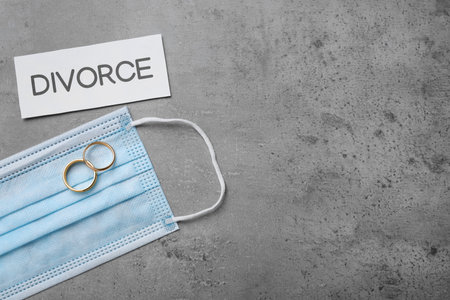 Flat lay composition with protective mask and wedding rings on gray table, space for text. Divorce during coronavirus quarantineの写真素材