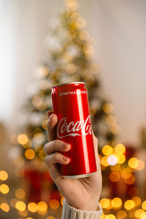 MYKOLAIV, UKRAINE - January 01, 2021: Woman with can of Coca-Cola against blurred Christmas tree indoors, closeupのeditorial素材