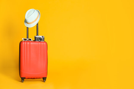 Travel suitcase with hat, camera and sunglasses on yellow background, space for text. summer holidaysの写真素材