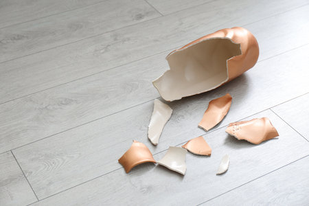 Broken golden ceramic vase on wooden floor, closeup. Space for textの写真素材