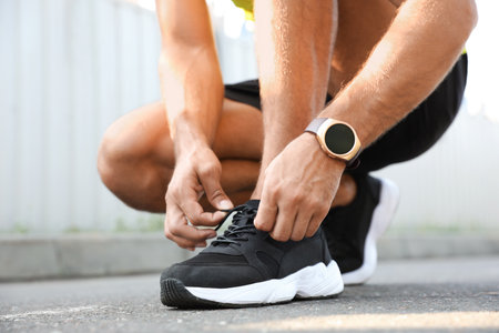 Man with fitness tracker tying shoelaces outdoors, closeupの写真素材