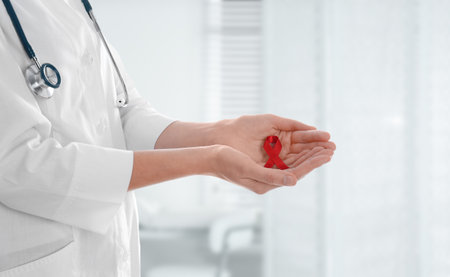 Doctor holding red awareness ribbon on blurred background, closeup. World AIDS disease dayの写真素材