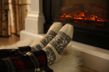 Woman in warm socks sitting near fireplace with burning wood at home, closeupの写真素材