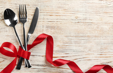 Cutlery set and red ribbon on white wooden background, flat lay with space for text. Valentine's Day dinnerの写真素材