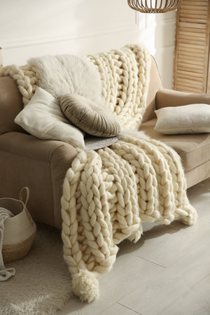 Beige sofa with knitted blanket and cushions in room. interior design