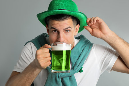 Man in St Patrick's Day outfit drinking beer on light gray backgroundの写真素材