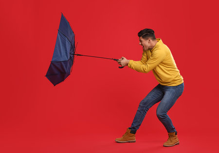 Emotional man with umbrella caught in gust of wind on red backgroundの写真素材