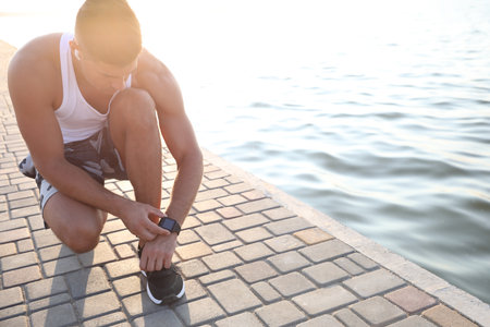 Man checking fitness tracker during training near river. Space for textの写真素材