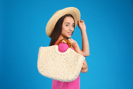 Young woman with stylish straw bag on light blue backgroundの写真素材