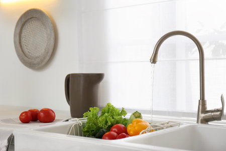Many fresh ripe vegetables under tap water in kitchen sinkの写真素材