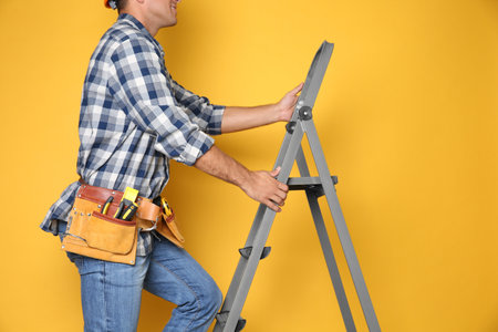 Professional builder climbing up metal ladder on yellow background, closeupの写真素材
