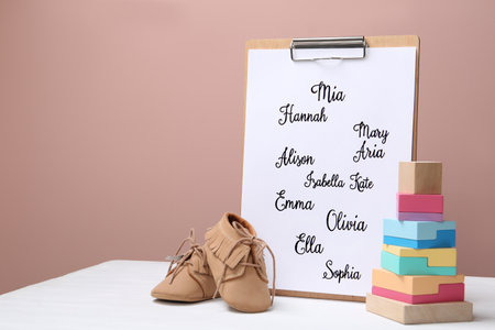 Clipboard with written different baby names, child's shoes and wooden toy on white wooden tableの写真素材