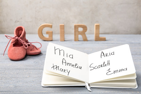 Notebook with written different baby names, child's shoes and wooden letters on gray wooden tableの写真素材