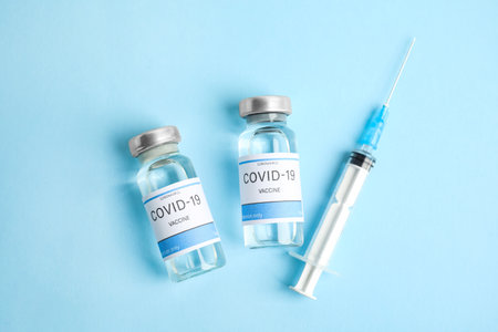 Vials with coronavirus vaccine and syringe on light blue background, flat layの写真素材