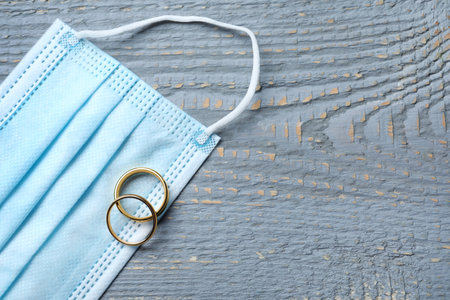 Protective mask and wedding rings on gray wooden table, flat lay with space for text. Divorce during coronavirus quarantineの写真素材