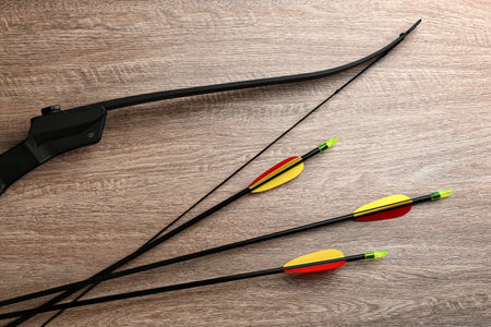 Plastic arrows and bow on wooden table, flat lay. archery sports equipment