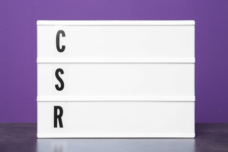 Light box with letters CSR on table against purple background. corporate social responsibilityの写真素材