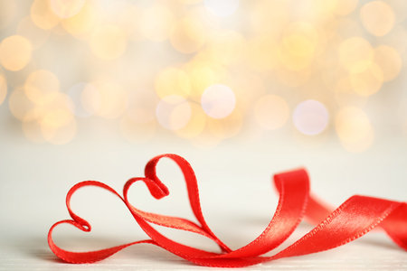 Two hearts made of red ribbon on table against blurred lights, space for text. St. Valentine's day cardの写真素材