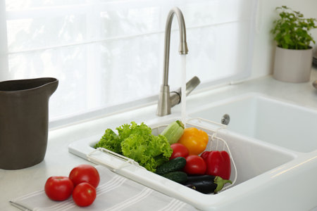 Many fresh ripe vegetables under tap water in kitchen sinkの写真素材