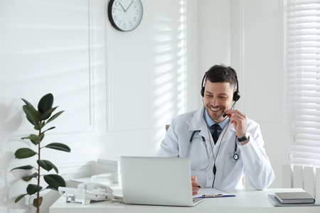 Doctor with headset consulting patient online at desk in clinic. Health service hotlineの写真素材