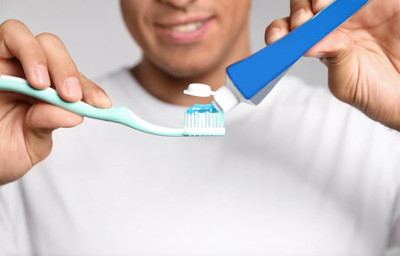 Man applying toothpaste on brush against light background, closeupの写真素材