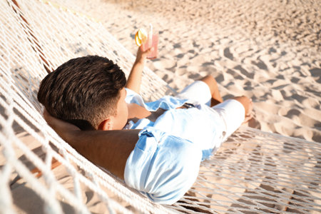 Man with refreshing cocktail relaxing in hammock on beachの写真素材