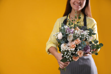 Florist holding beautiful wedding bouquet on yellow background, closeup. Space for textの写真素材