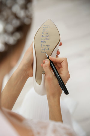 Young bride writing her single friends names on shoe indoors, closeup. wedding superstitionの写真素材