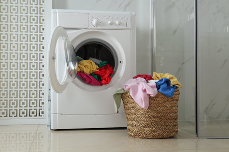 Wicker laundry basket with different clothes near washing machine in bathroomの写真素材
