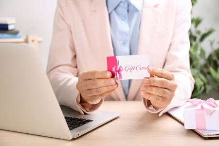 Woman with gift card and laptop at table indoors, closeupの写真素材