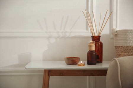 Oil reed diffuser and candles on wooden table near white wall, space for text. interior decorの写真素材