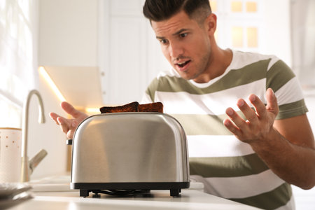Emotional man near toaster with slices of burnt bread in kitchenの写真素材