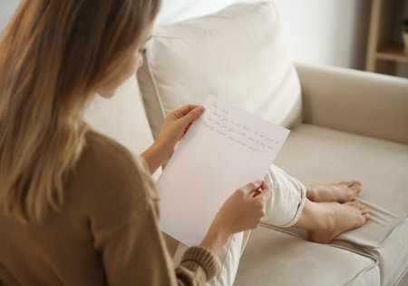 Woman reading letter on sofa at home, closeupの写真素材
