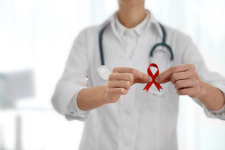 Doctor holding red ribbon on blurred background, closeup. AIDS awareness monthの写真素材