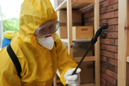 Pest control worker in protective suit spraying pesticide indoorsの写真素材