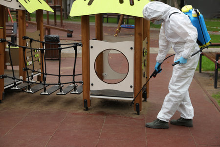 Woman wearing chemical protective suit with disinfectant sprayer on playground. Preventive measure during coronavirus pandemicの写真素材