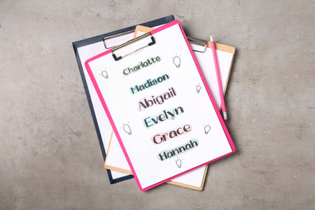 Clipboards with different baby names and pencil on gray table, top viewの写真素材