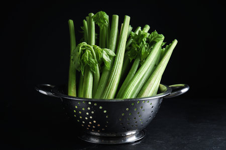 Fresh green celery in colander on black tableの写真素材
