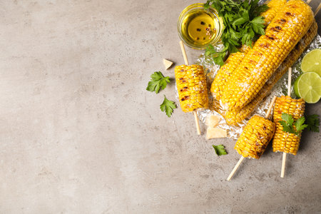 Delicious grilled corn cobs on gray table, flat lay. Space for text