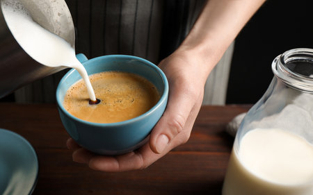Woman pouring milk into cup of hot coffee, closeupの写真素材