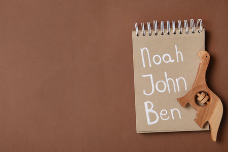 Notebook with list of baby names and wooden toy on brown background, top view. Space for textの写真素材
